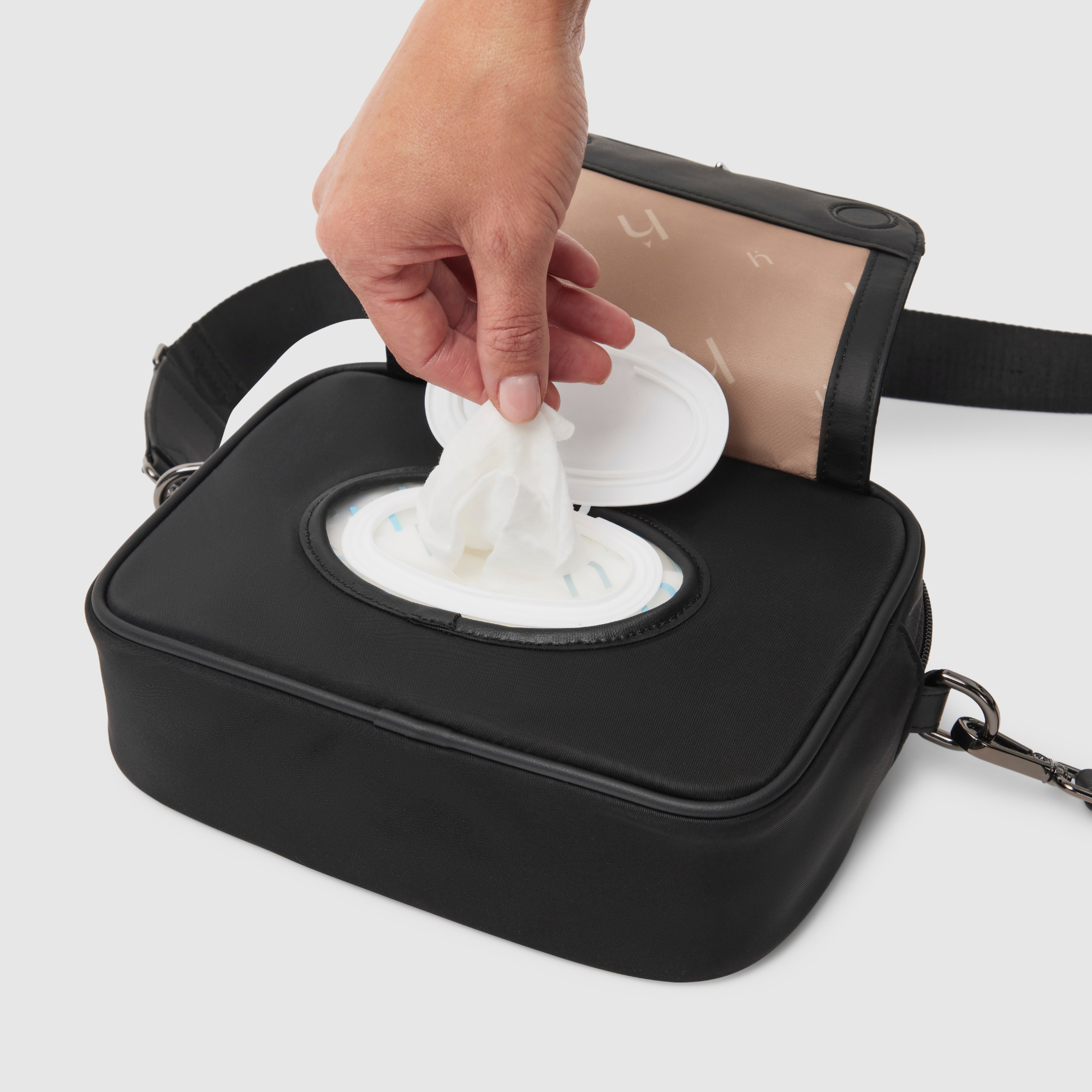 hand pulling baby wipes from wipes dispenser of crossbody baby bag